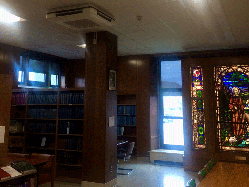 Ceiling-mounted Daikin VRV unit in wood-paneled library with bookshelves, table, and stained glass.