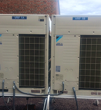 Two Daikin VRV IV units on rooftop beside brick building with visible piping connections.